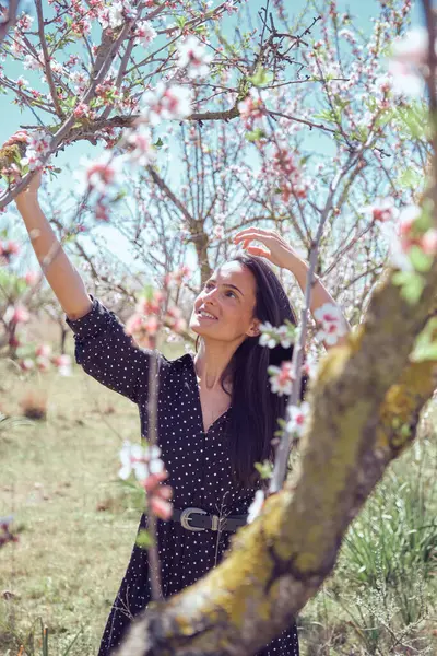 咲くピンクの花と木の枝に触れるベルトの乾いた夏のドレスの笑顔の女性と雲のない青空の下でそれに成長する葉 — ストック写真