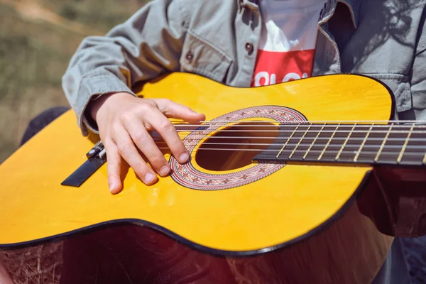 草の草の牧草地でアコースティックギターを演奏カジュアルな服で作る匿名の子供の上から晴れた日に — ストック写真