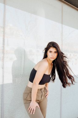 Güzel kadın duvarın yanında duruyor.