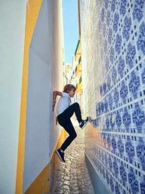 Kentin dar sokaklarında bulunan dekoratif renkli bir bina duvarına tırmanmaya çalışan bir çocuğun tüm vücudu kenar manzaralı.