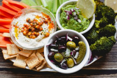 İştah açıcı sağlıklı humus yeşil sosu havuç, salatalık ve yeşil brokolili salatalık dilimlenmiş beyaz limon ile ahşap masada.