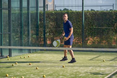 Spor giyim kuşağında spor sahasında raketle, yaz günü antrenman sırasında ağla Padel oynayan aktif bir erkek vücudu.