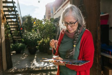 Yazın güneşli bir günde arka bahçede duran boya paleti ve fırçalarla odaklanmış son sınıf kadın sanatçı.