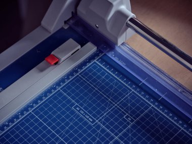 Kitap ciltleme atölyesinde masanın üzerine mavi grafik kağıdı yerleştirilmiş profesyonel modern kesim makinesinin yüksek açılı yakın çekimi