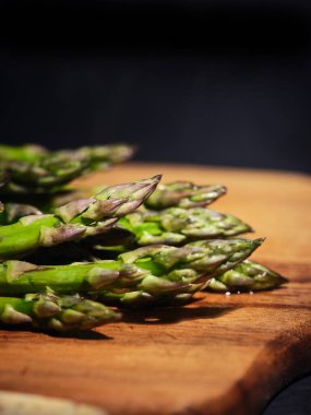 Sağlıklı beslenme için taze taze taze kuşkonmaz. Mutfaktaki siyah arka planla ahşap doğrama tahtasına yerleştirilmiş.