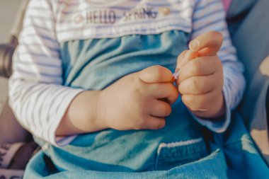 Güneşli bir günde sokakta gezen lolipop beyazı paketini açan sıradan kıyafetli isimsiz bir kız.