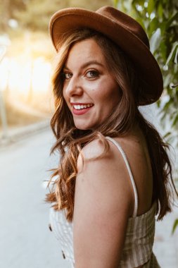 Çekici, uzun saçlı, yeşil yaprakların ortasında şapkalı mutlu kadın.