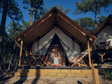 Nilüfer çiçeğinde oturan uzak bir anne. Namaste elleri ile tahta terasta oturuyor. Oğlu da kırsal alanda inşa ediyor.