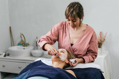 Modern güzellik salonundaki cilt bakımı sırasında kadın müşterinin yüzüne nemlendirici yüz maskesi uyguluyor.