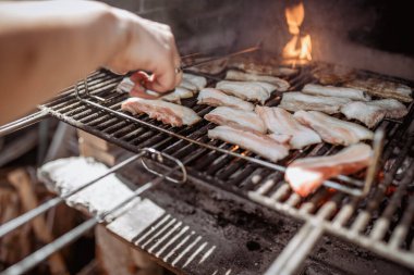 Barbeküde domuz pastırması pişiren insan.