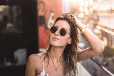 Uzun saçlı, yaz elbisesi giyen, güneş gözlüğü takan çekici ve düşünceli bir model.