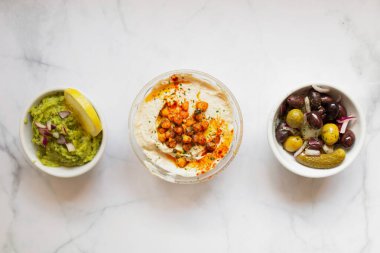 Yukardan gelen lezzetli sağlıklı humus yeşil sosu soğan, tuzlu salatalık dilimlenmiş limonla süslenmiş masa üstünde beyaz kaseler.