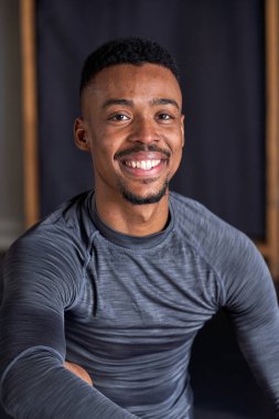 Dans akademisinde spor kıyafetleri, terlikleri ve balesi olan zenci bir çocuğun fotoğrafı.