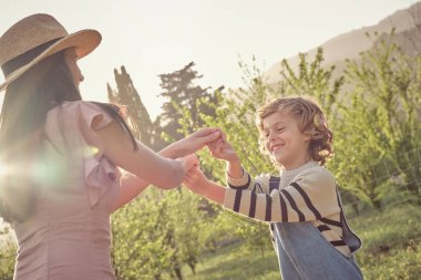 Oğlu kırsalda dinlenirken, günlük kıyafetleri ve şapkası olan mutlu genç bir kadın.