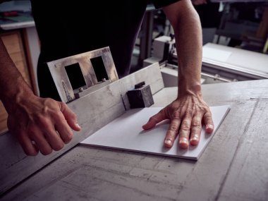 Masanın yanında duran, kağıt çarşaflı ahşap tezgah kullanan ve ölçüm yapan isimsiz bir adamdan.