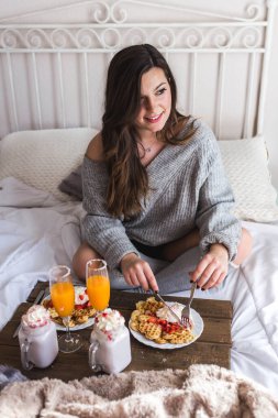 Tahta tepsinin yanında, nefis kremalı Belçika waffle 'ları, bir bardak taze meyve suyu ve milkshake ile çekici bir kadın oturuyor.