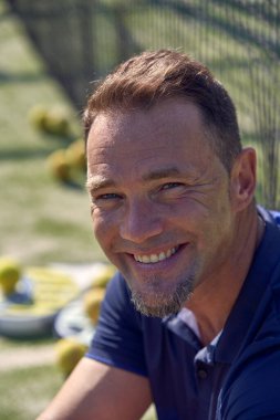 Güneşli yaz gününde Padel antrenmanında ağların yanında dikilirken kameraya bakan aktif erkek.