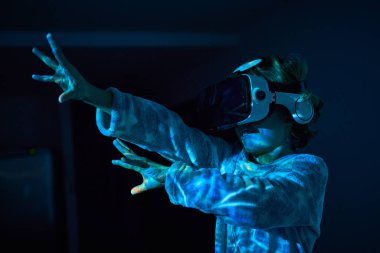 Sıcak pijama giymiş sevimli bir çocuk kollarını açmış ve gülümsüyor. Karanlık odada kulaklık takmış çağdaş gözlüklerle sanal gerçekliği yaşıyor.