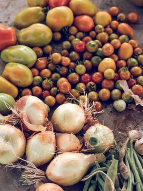 Olgun yeşil ve kırmızı domates yığınının tepesinden olgun soğan yüzbaşısı ve yere konmuş çalı fasulyesi.