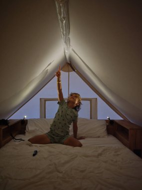 Gece vakti evde Mansard 'da rahat bir yatakta otururken tavanda gölge yapan sevimli çocuk.