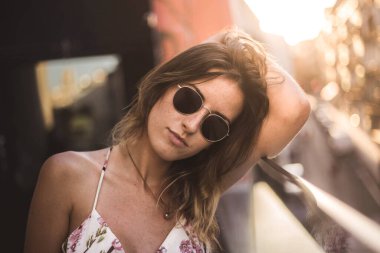 Uzun saçlı, yaz elbisesi giyen, güneş gözlüğü takan çekici ve düşünceli bir model.