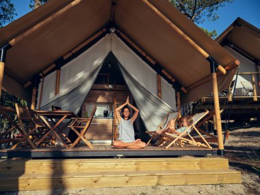 Nilüfer çiçeğinde oturan tüm kadın vücudu, oğlunun yanındaki terasta yoga sırasında ellerinizi başınızın üstünde namaste jestine sıkıştırarak poz verir.