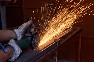 Profesyonel eldiven giyen tanınmayan bir zanaatkar, doğramacıda elektrikli yapboz kullanarak metal kesme işlemi sırasında tezgahta duruyor.