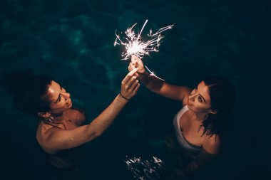 Havuz kenarında havai fişek yakan neşeli arkadaşlar 