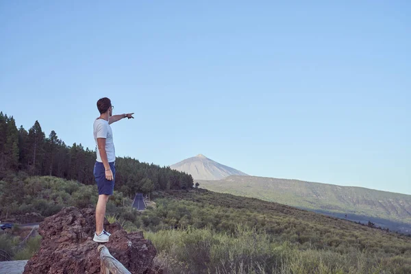 夏の日に自然の中で旅行中に手すりに立っている間に山を指す男性観光客の完全なボディサイドビュー — ストック写真