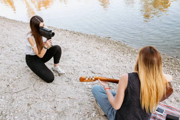 Young woman shooting friend playing guitar