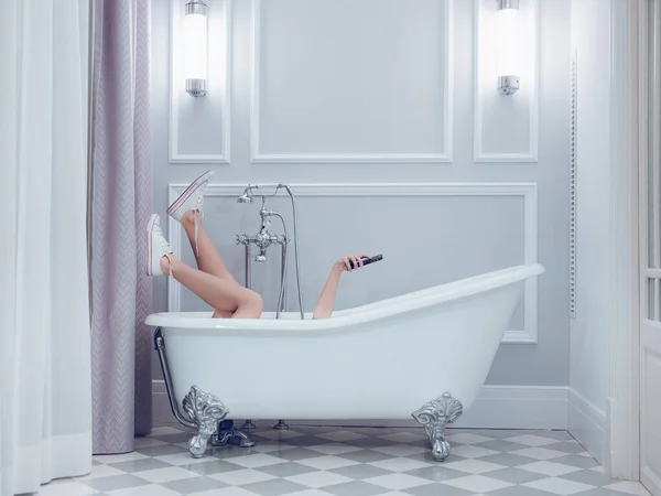 穿着运动鞋 在白色浴缸里放松 在轻便浴室里使用手机的难以辨认的女人的侧视图 — 图库照片