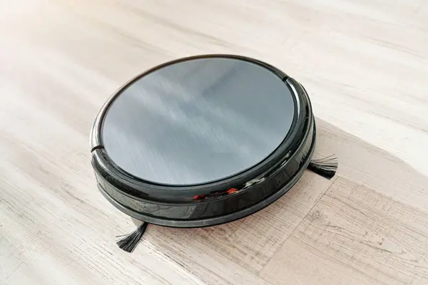 From above of black robotic vacuum cleaner placed on light floor in room in apartment