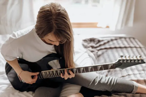 サイドビューの若いですブルネット女性演奏ギターオンベッド — ストック写真