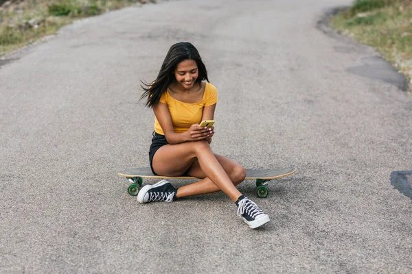 Ethnic Female Browsing Smartphone While Sitting Longboard Asphalt Road — Stock Photo, Image