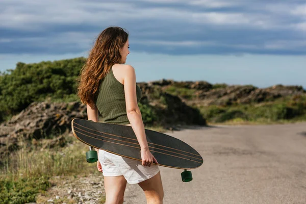 无法辨认的年轻女子滑板手的背影 她在山路和海路上散步 — 图库照片