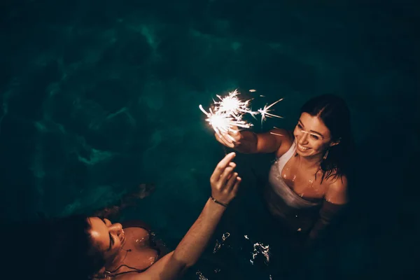 Cheerful friends burning sparkles near pool