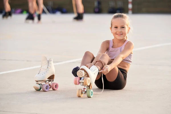 フルボディの幸せなスポーツ女の子見ますカメラを置きながら上のクワッドローラースケート中にトレーニング上の遊び場 — ストック写真