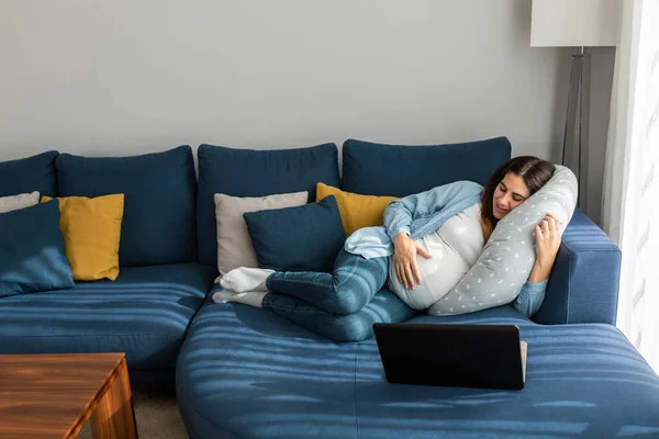 快乐的孕妇躺在舒适的沙发上 一边在上网本上看有趣的视频 一边在家里放松 — 图库照片