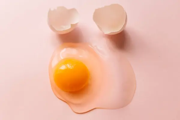 上から黄色の黄身とピンクの背景に卵殻で割られた卵 — ストック写真