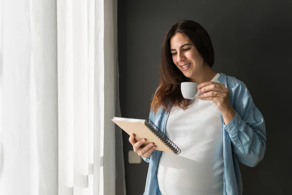 Cheerful Pregnant Female Cup Drink Notepad Standing Room Home — Stock Photo, Image