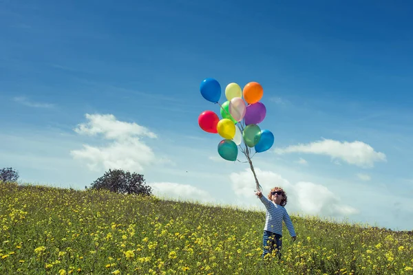 Μικρό Παιδί Γυαλιά Ηλίου Κρατώντας Πολύχρωμα Μπαλόνια Ενώ Στέκεται Ανθισμένα — Φωτογραφία Αρχείου