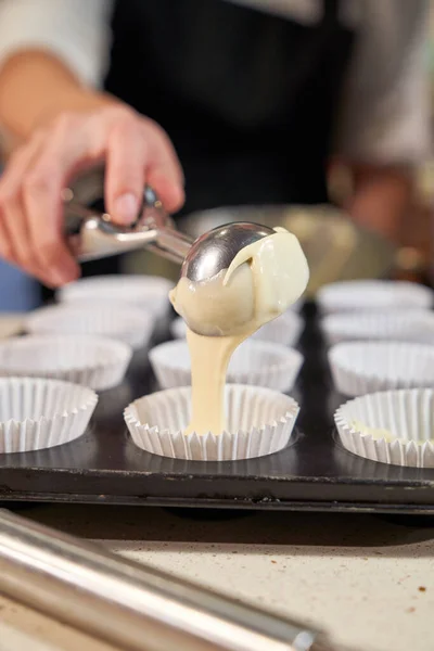 ライトキッチンで甘いカップケーキを焼く準備しながら 金属のスクープからバッテリーを注ぐ匿名の人をクロップ — ストック写真