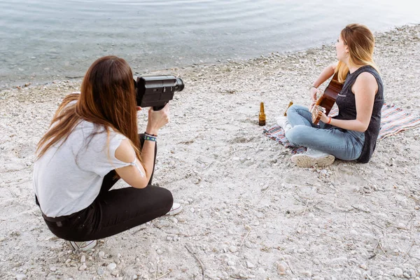 Young woman shooting friend playing guitar