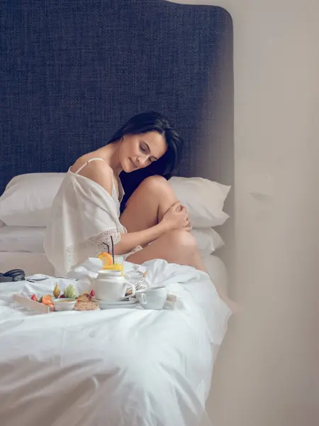 新鮮なおいしい朝食と豪華なホテルで朝を楽しみながらトレイ近くのベッドでリラックスしたシルクナイトウェアの穏やかな女性の側面 — ストック写真