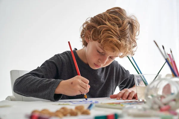 Συμπυκνωμένο Αγόρι Ζωγραφική Paintbrush Λευκό Χαρτί Πολύχρωμα Χρώματα Ενώ Κάθεται — Φωτογραφία Αρχείου