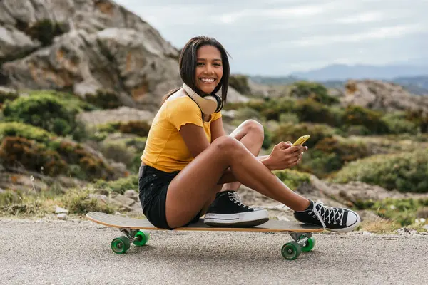 Etnisk Kvinna Surfa Smartphone Medan Sitter Longboard Asfalterad Väg — Stockfoto