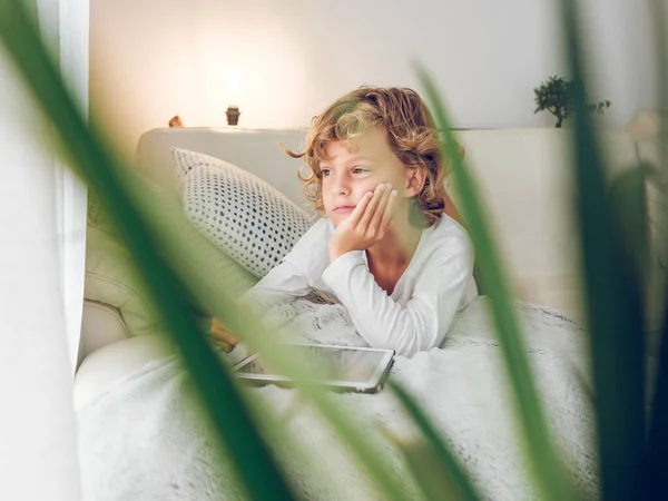 タブレットとソファーに横たわり 窓と夢を見ている愛らしいペンシルベニアの少年 — ストック写真