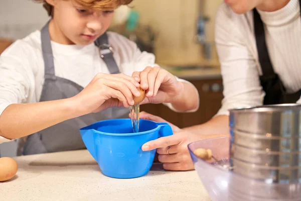 Chłopiec Fartuchu Dodając Surowe Jajko Plastikowego Pojemnika Gotowania Ciasta Podtrzymującą — Zdjęcie stockowe