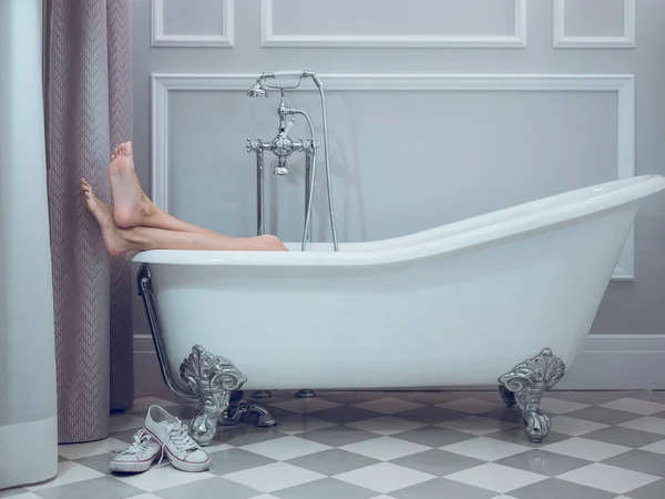 无法辨认的赤脚女子躺在白色浴缸里 双腿伸出 交叉在酒店浴室里 — 图库照片