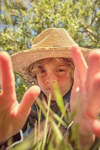 Cute Little Boy Słomkowym Kapeluszu Patrząc Aparat Docierając Rąk Zielonej — Zdjęcie stockowe